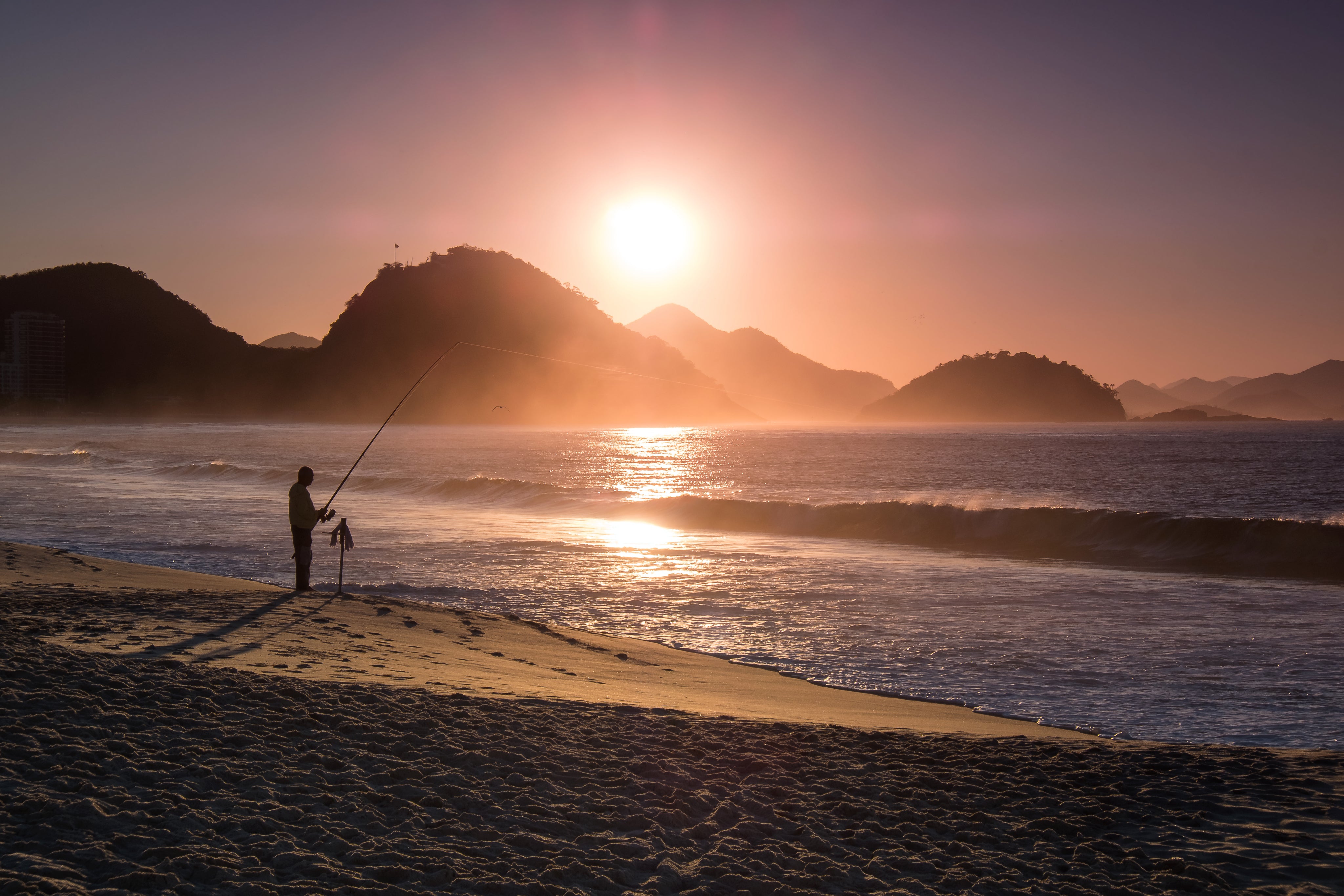 person-fishing-on-the-beach-is-silhouetted-at-sunset.jpg